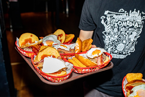 A person's arm holding a tray of breakfast baps filled with eggs, bacon and sausage burgers.