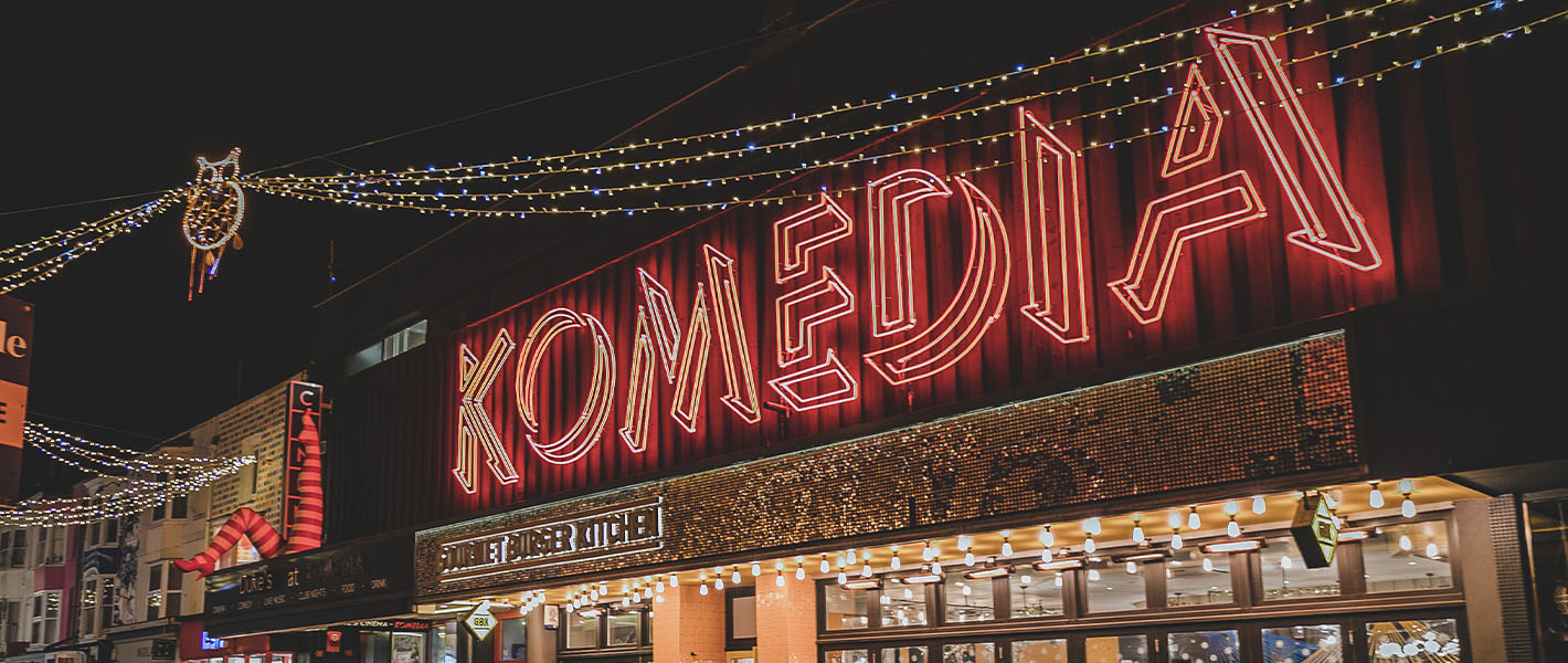 An image of the front of the Komedia building with the Komedia neon sign.